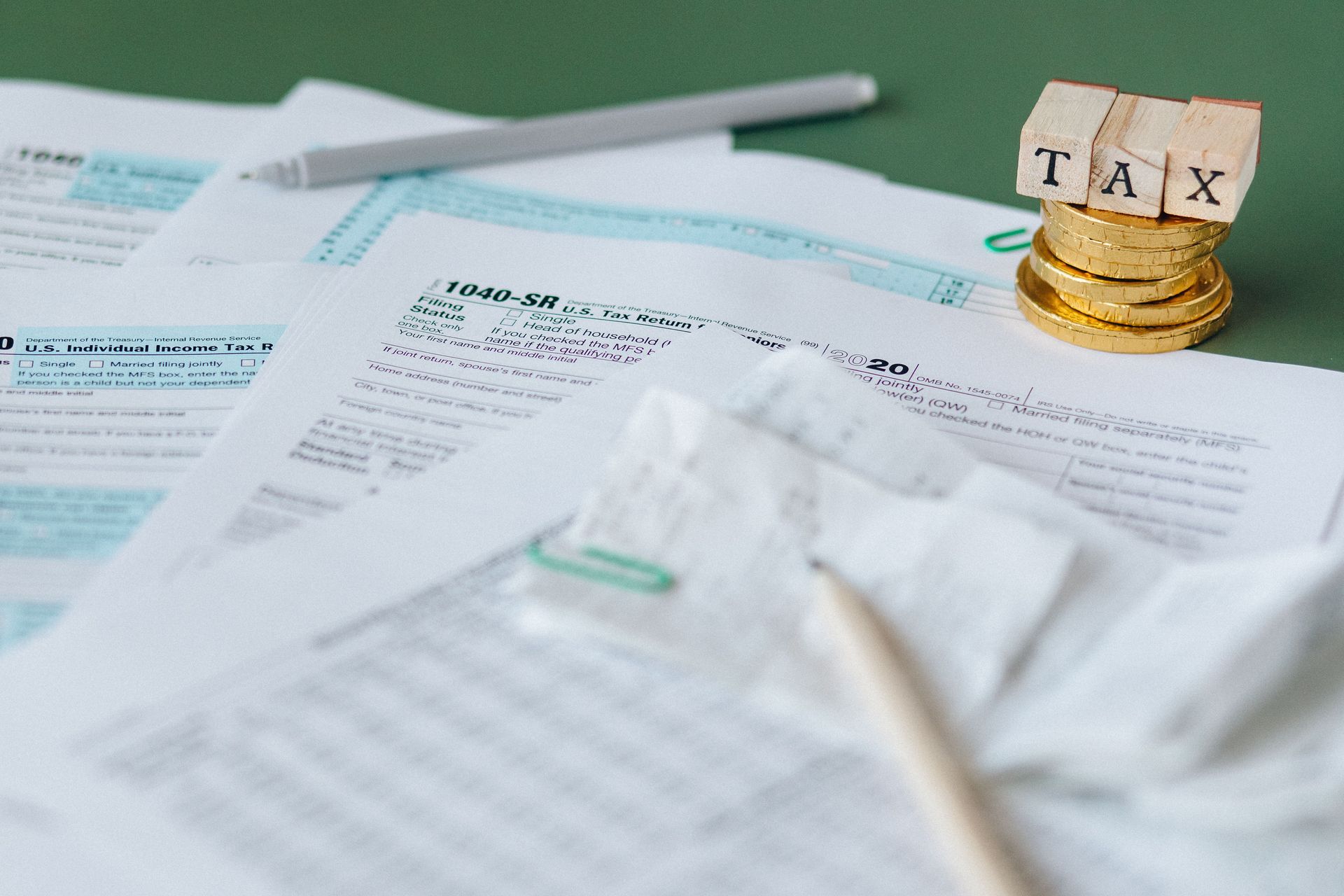 Stack of tax forms and coins with a 'TAX' stamp, symbolizing finance and accounting.