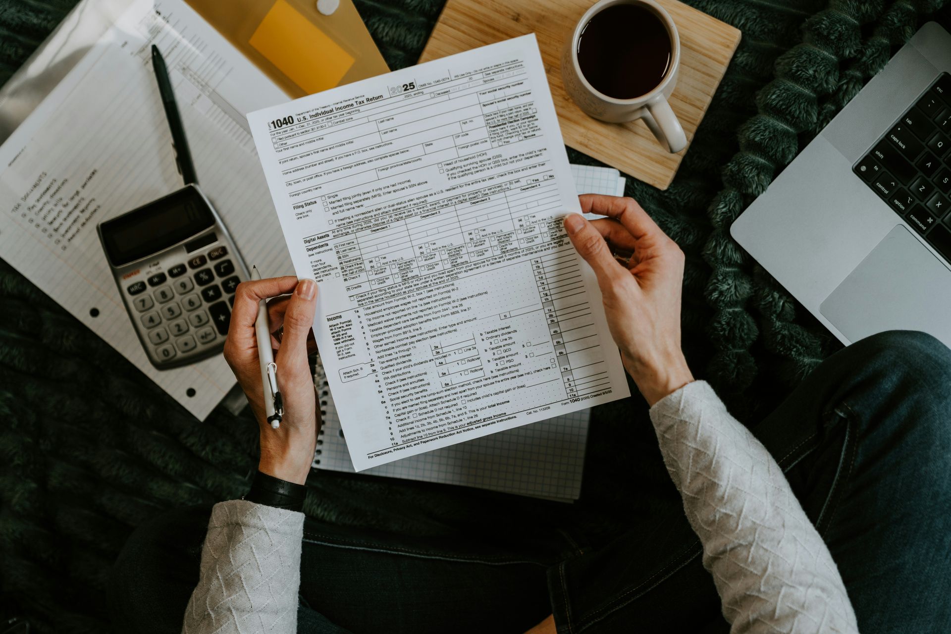 Hands holding tax forms with calculator and laptop